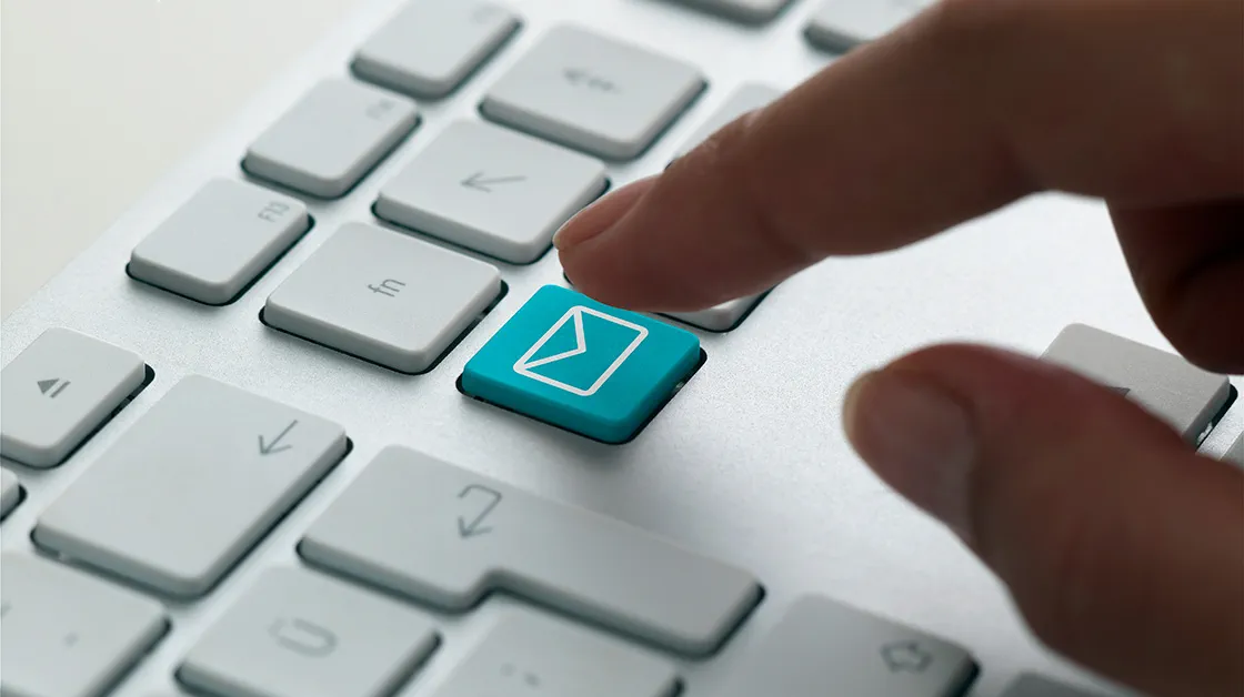 Computer keyboard with finger hovering over a shortcut button to send email - the button is blue and has an envelope symbol