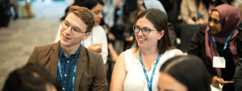two young professionals male and female with glasses on wearing lanyards sitting down at a conference