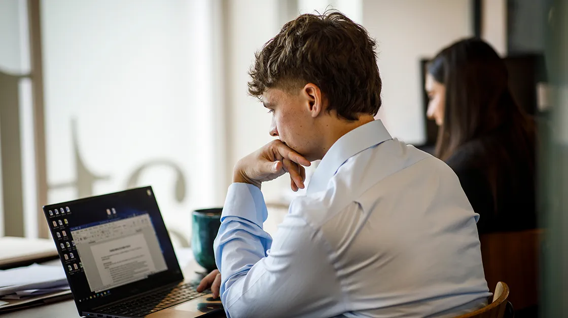 A solicitor sits in an office, reading a report on a laptop.