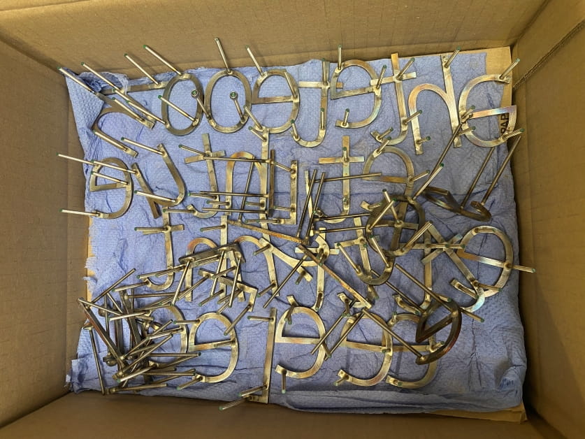 A cardboard box lined with blue tissue and covered in steel letters that are being prepared for an artwork