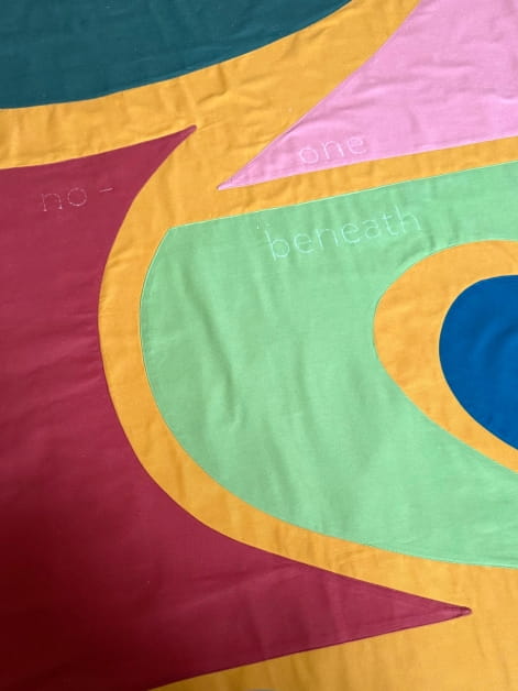 A close up of Helen Cammock's fabric banner featuring abstract shapes in green, pink, blue, teal and red against a yellow backdrop.