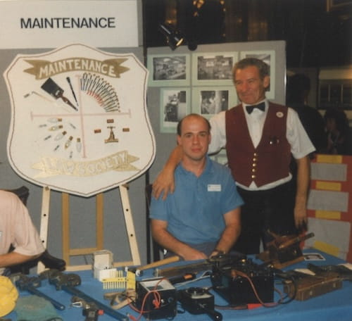 Richard Hopkins with another person, at a table with a sign that reads 'maintenance'.