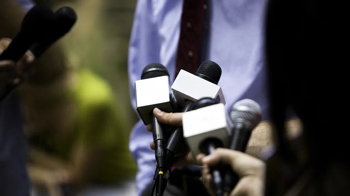 Microphones are held to a man in a suit, as if he is being interviewed