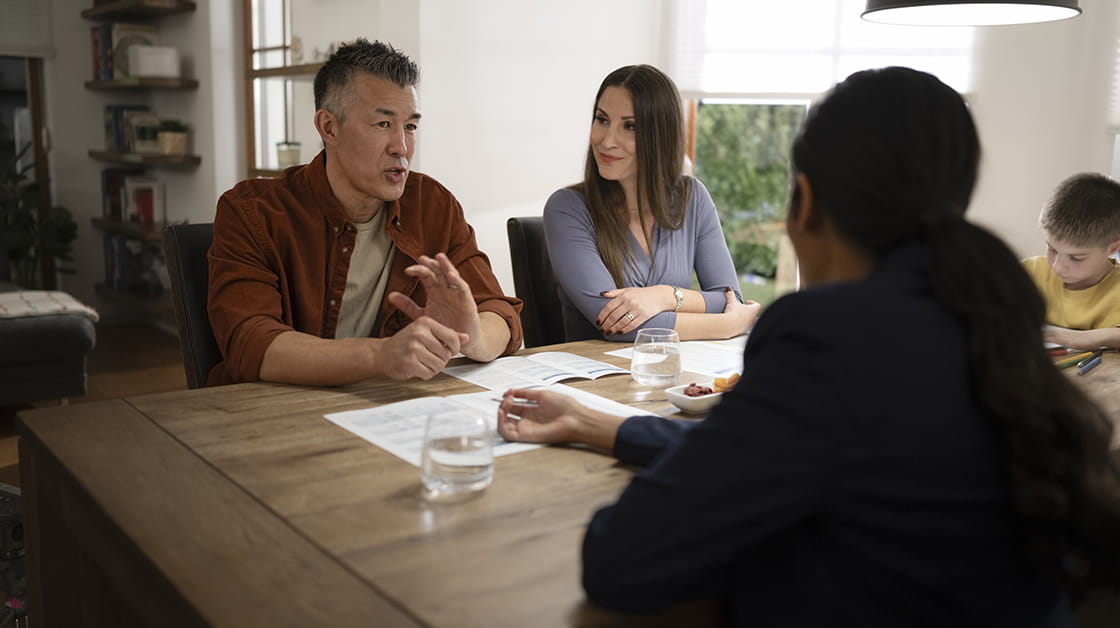 A smiling family sits around a table in conversation with a professional.