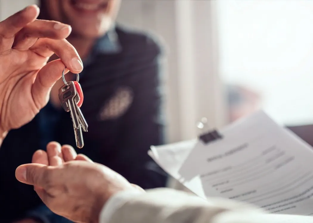 Estate agent sitting at the desk by the window and passing keys to his client in the office